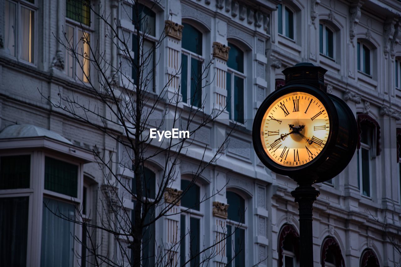 Low angle view of illuminated clock against building at dusk