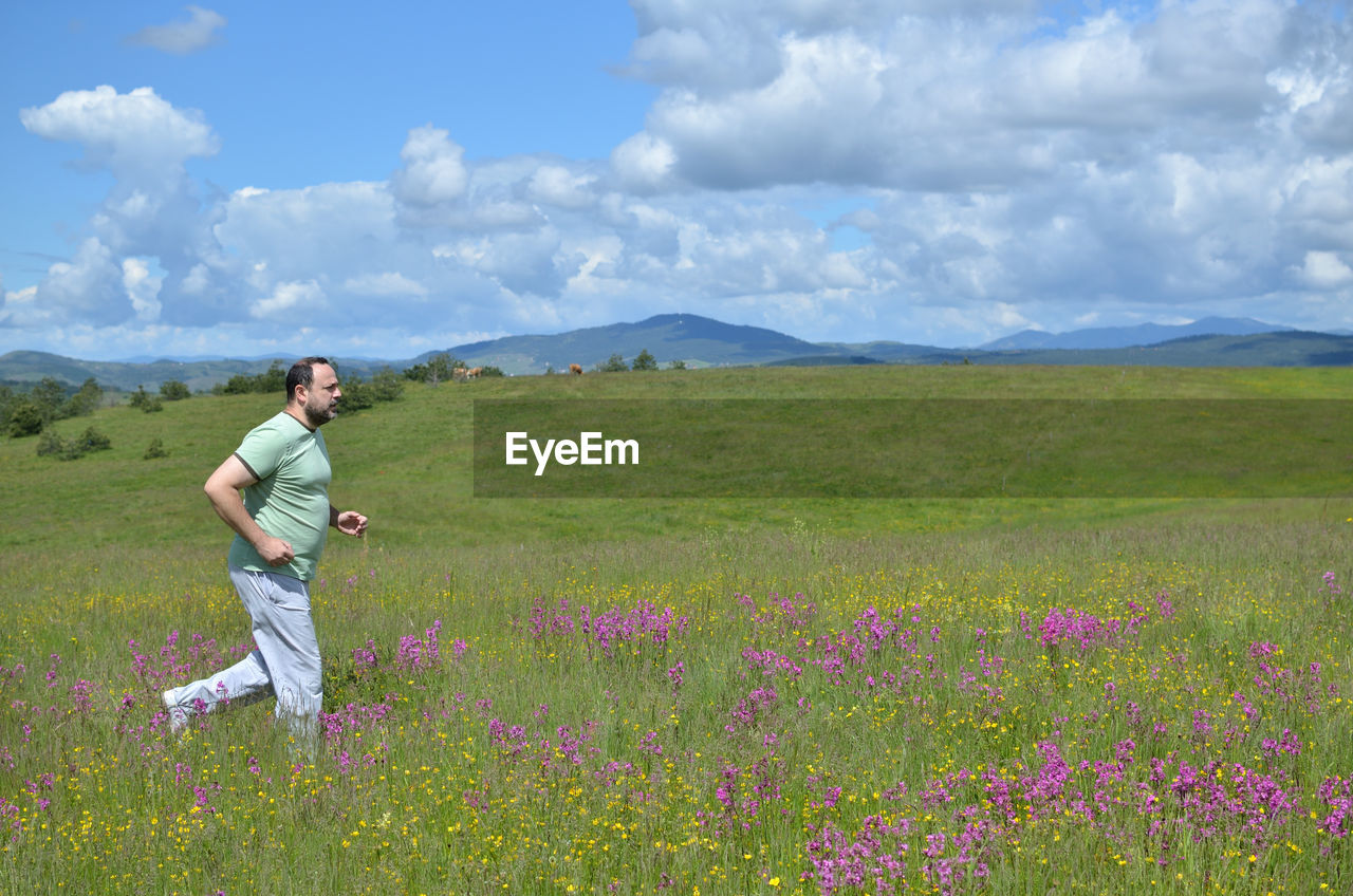 Man running in nature on a cloudy day in springtime, with hill and clouds in background