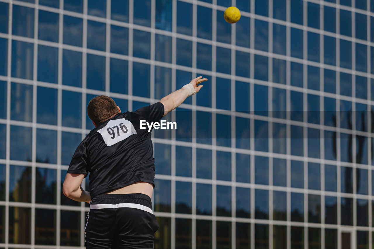 Male athlete shot put on background glass facade