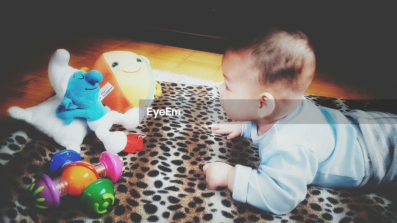 Baby boy looking at toys while lying on animal patterned blanket