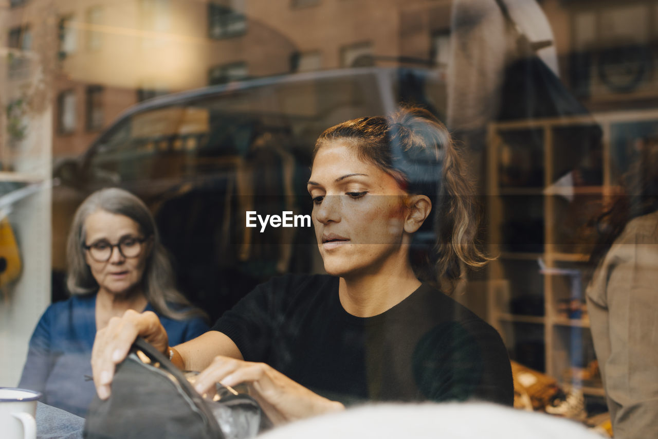 Female colleagues seen through glass working in clothing store