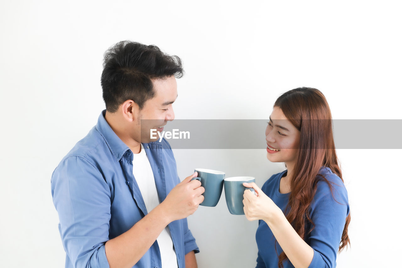 Loving couple holding coffee cups while standing against white background