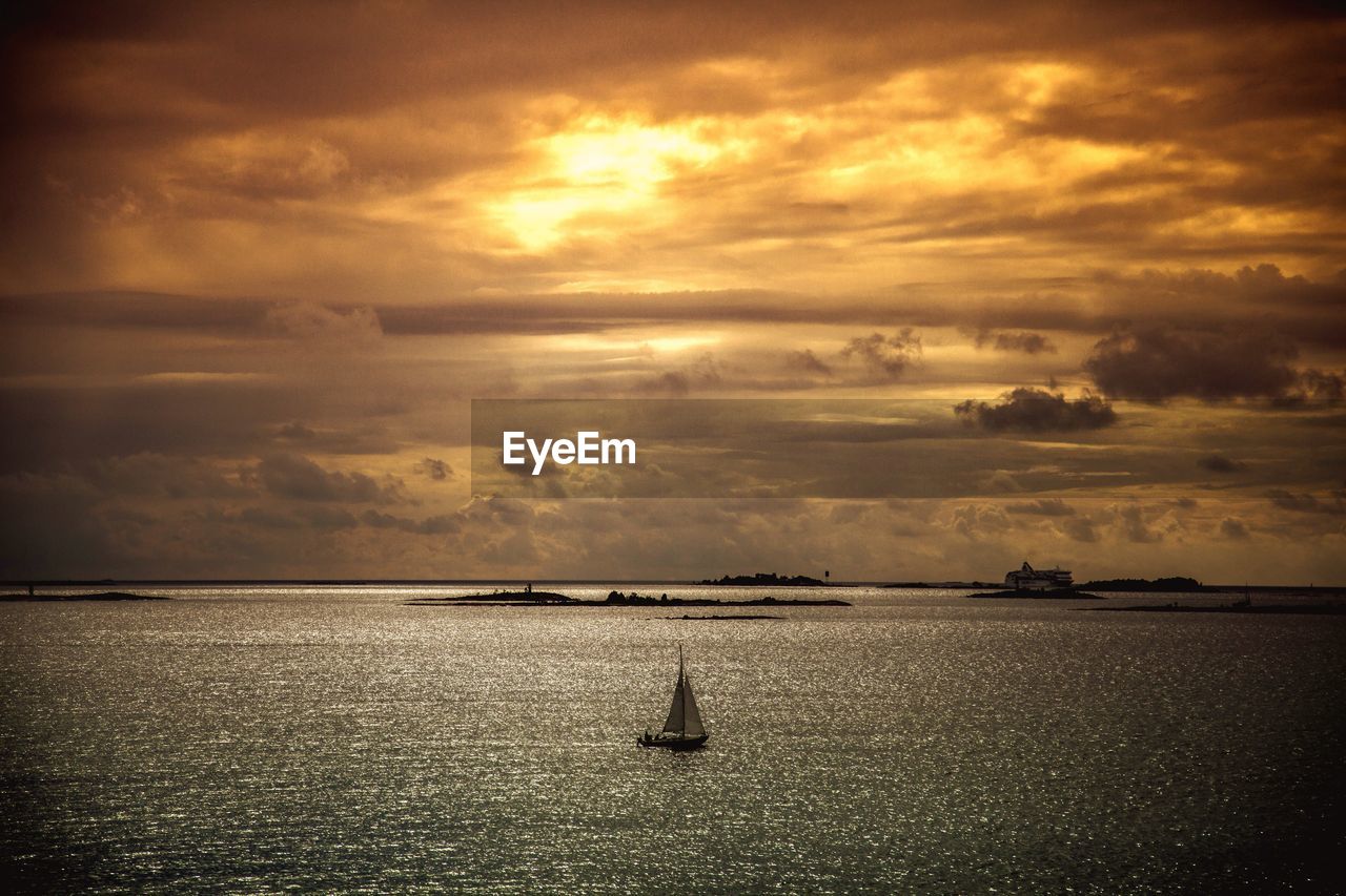 Boat sailing in sea against cloudy orange sky during sunset