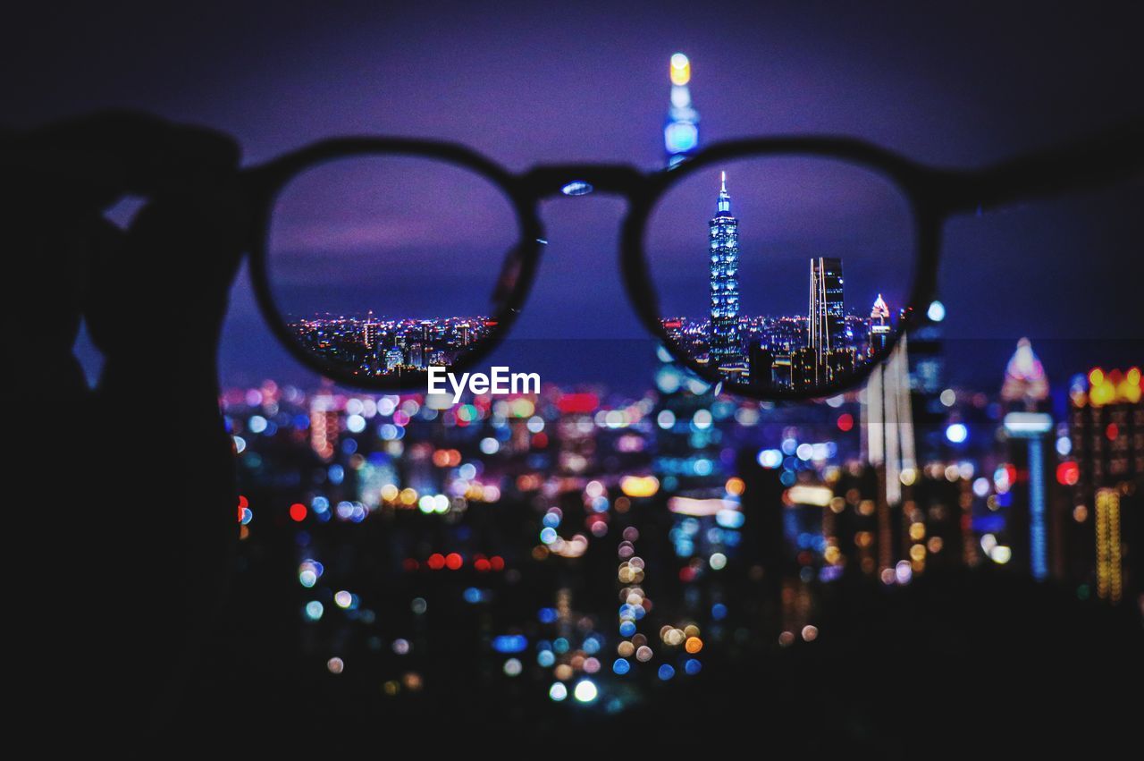 Illuminated buildings in city seen through eyeglasses at night