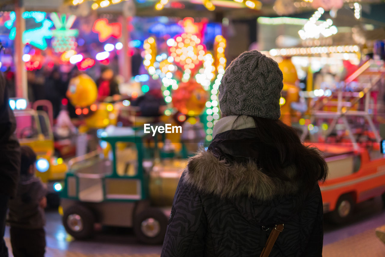 Rear view of woman against illuminated rides at night