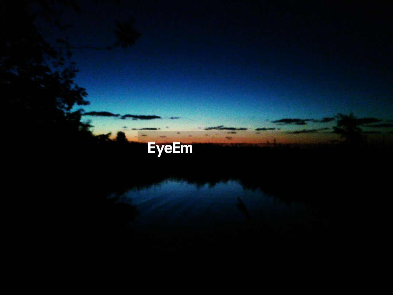 SILHOUETTE LANDSCAPE AGAINST CALM LAKE AT SUNSET