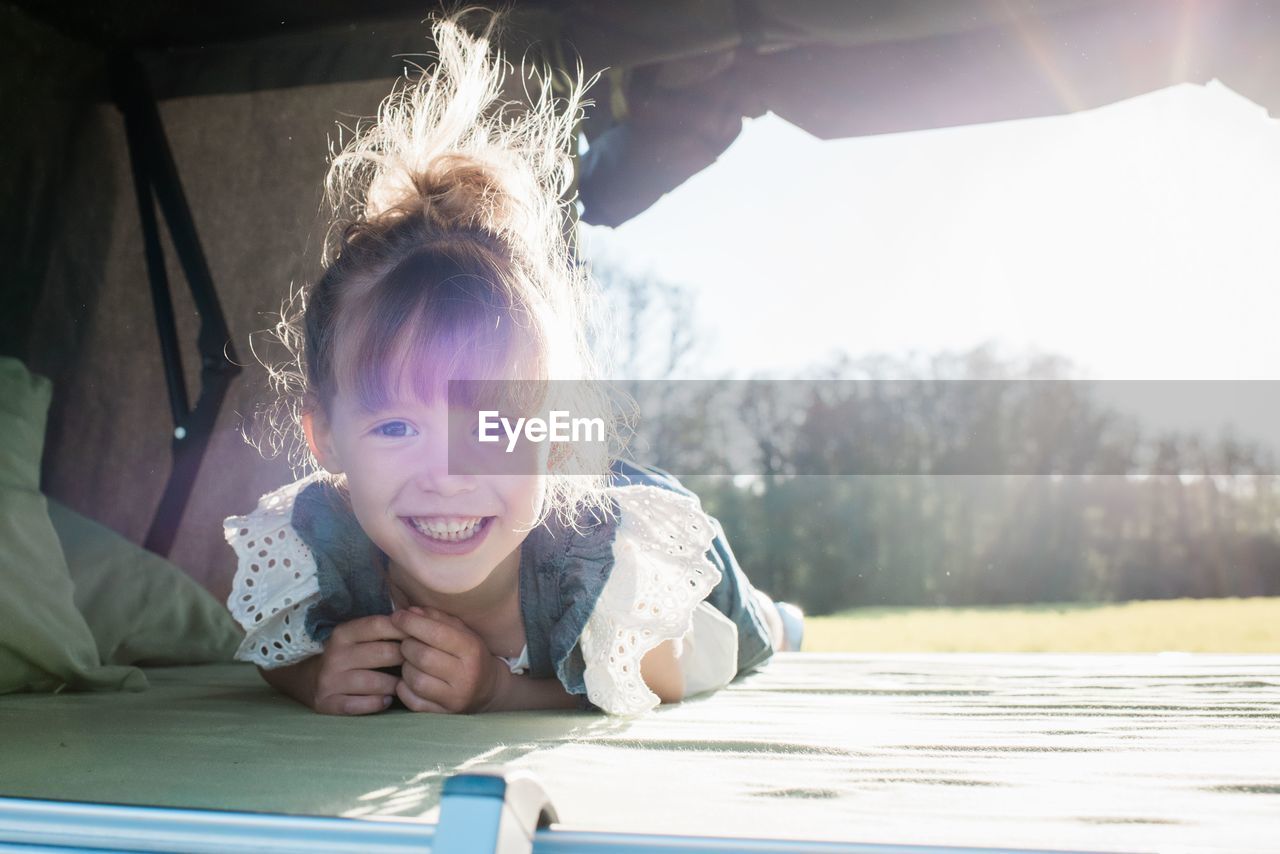 Portrait of a young girl sat in a roof top tent smiling at sunset