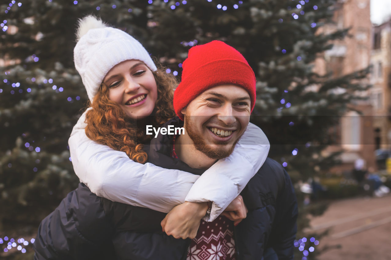 Loving boyfriend and girlfriend are hugging happily near a big city christmas tree