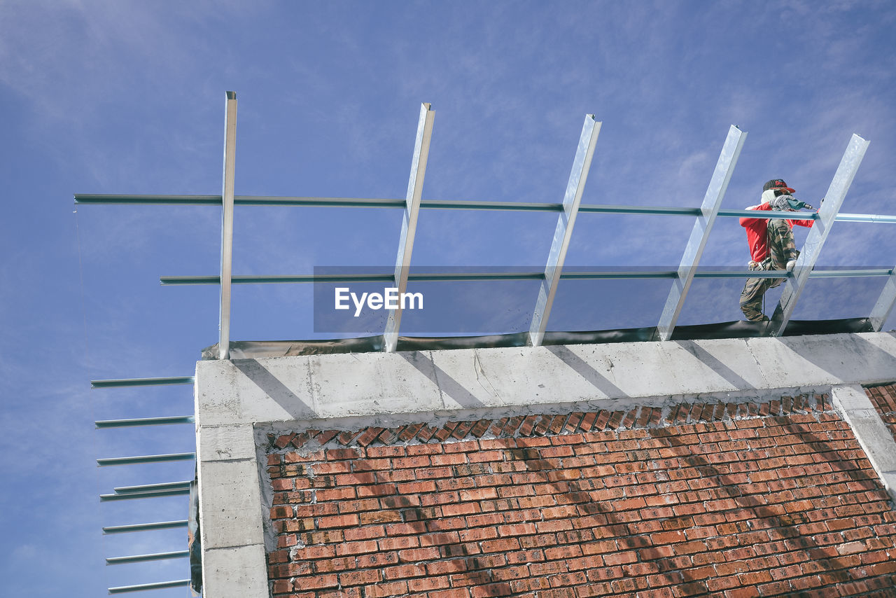 Low angle view of mason working at construction site against sky