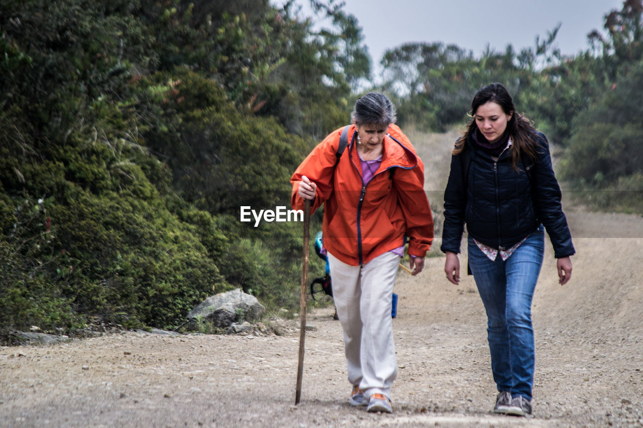 Full length of mother and daughter walking on hill in forest