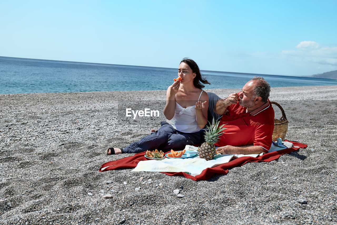 Middle aged couple having a picnic at the seaside with fresh exotic fruit. spring, summer time