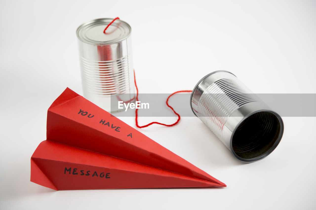 High angle view of red paper plane with text by tin can phone against white background