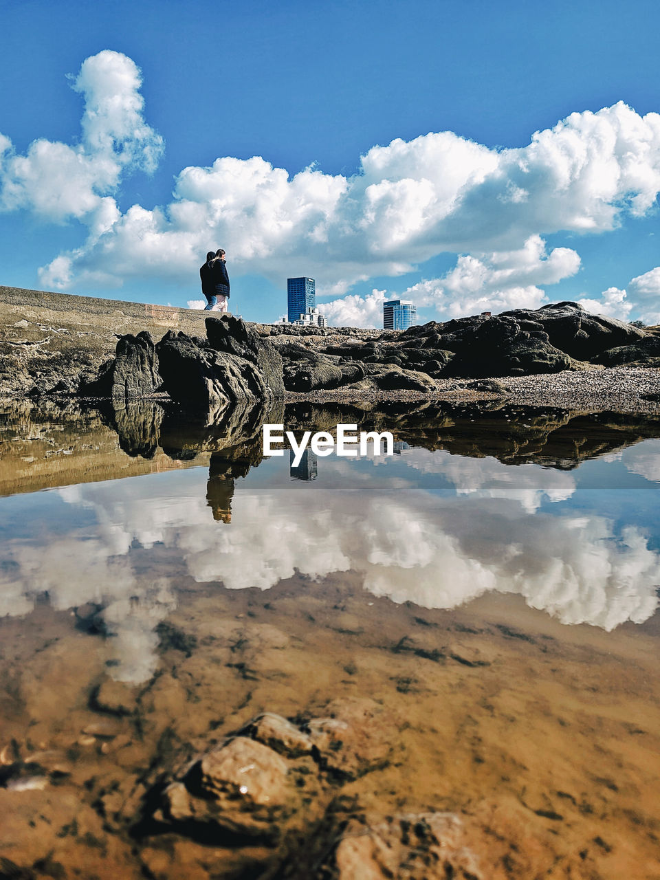 reflection, sky, water, cloud, sea, nature, landscape, coast, rock, mountain, environment, scenics - nature, land, day, travel destinations, shore, beauty in nature, one person, travel, outdoors, architecture, blue, tranquility, horizon, adult, men, beach, leisure activity, ocean, natural environment, full length, terrain