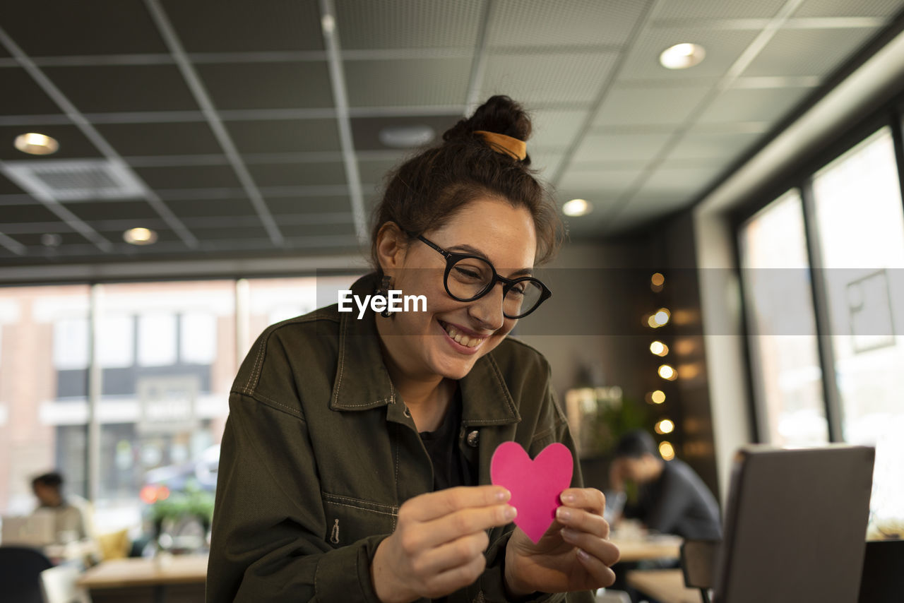 Smiling woman in cafe holding paper heart