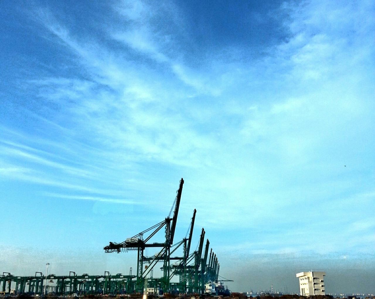 Row of cranes at commercial dock against sky