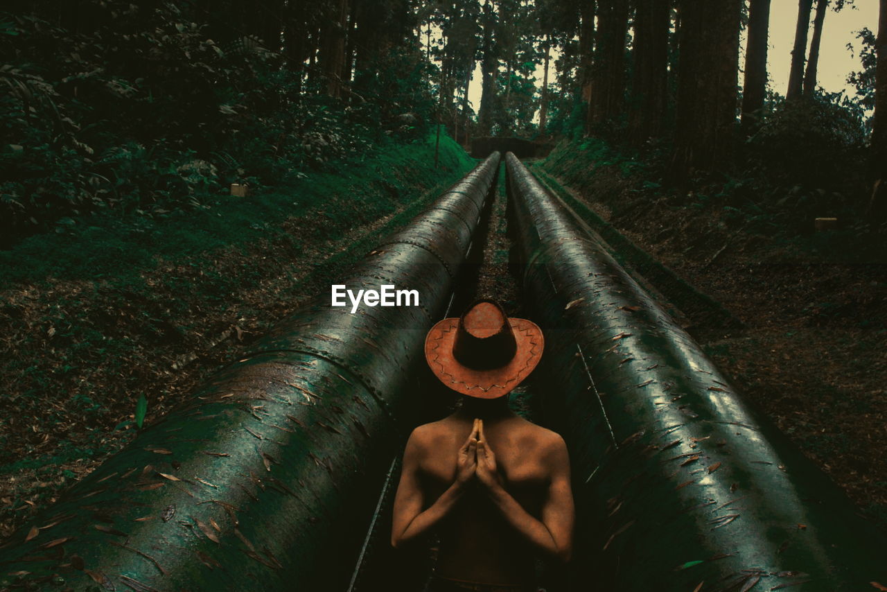 Woman doing yoga amidst water pipes in forest