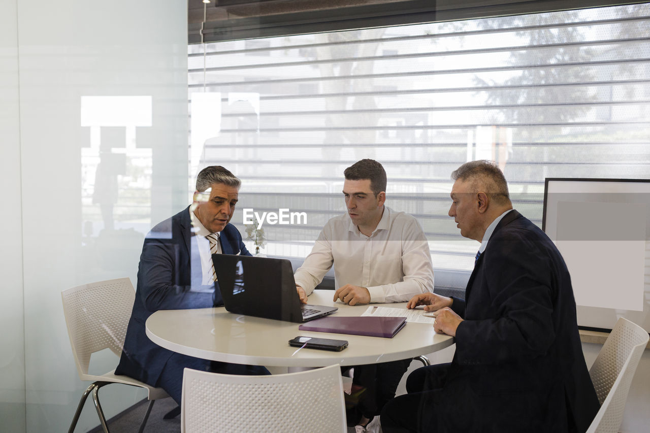 Businessman discussing over laptop with colleagues sitting at desk in office