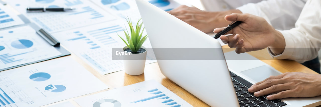 Cropped hand of business people working with laptop in office