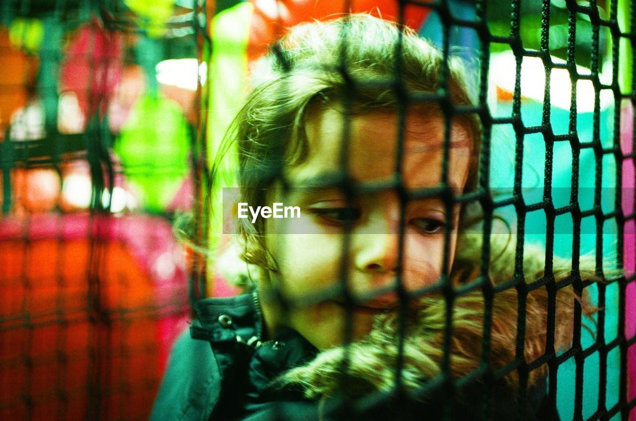 CLOSE-UP PORTRAIT OF A BOY LOOKING THROUGH FENCE IN PARK