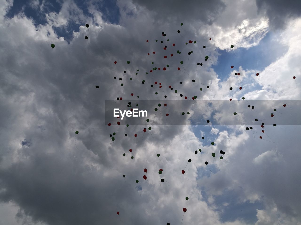 Low angle view of balloons flying against cloudy sky