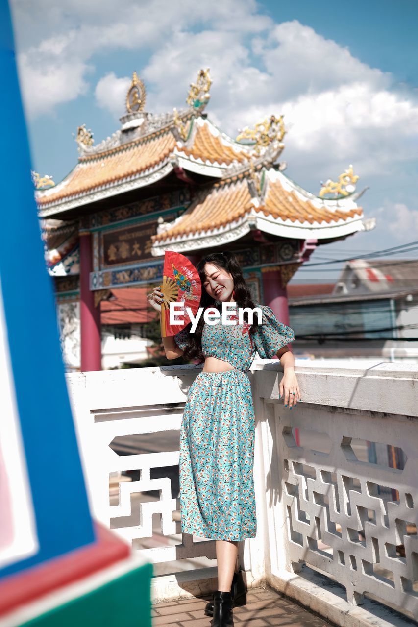 Portrait of woman in blue modern cheongsam holding a red fan at chinese temple 