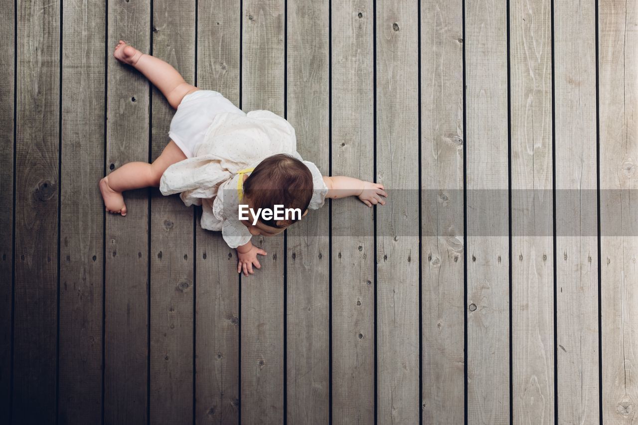 High angle view of baby girl crawling on wooden floor