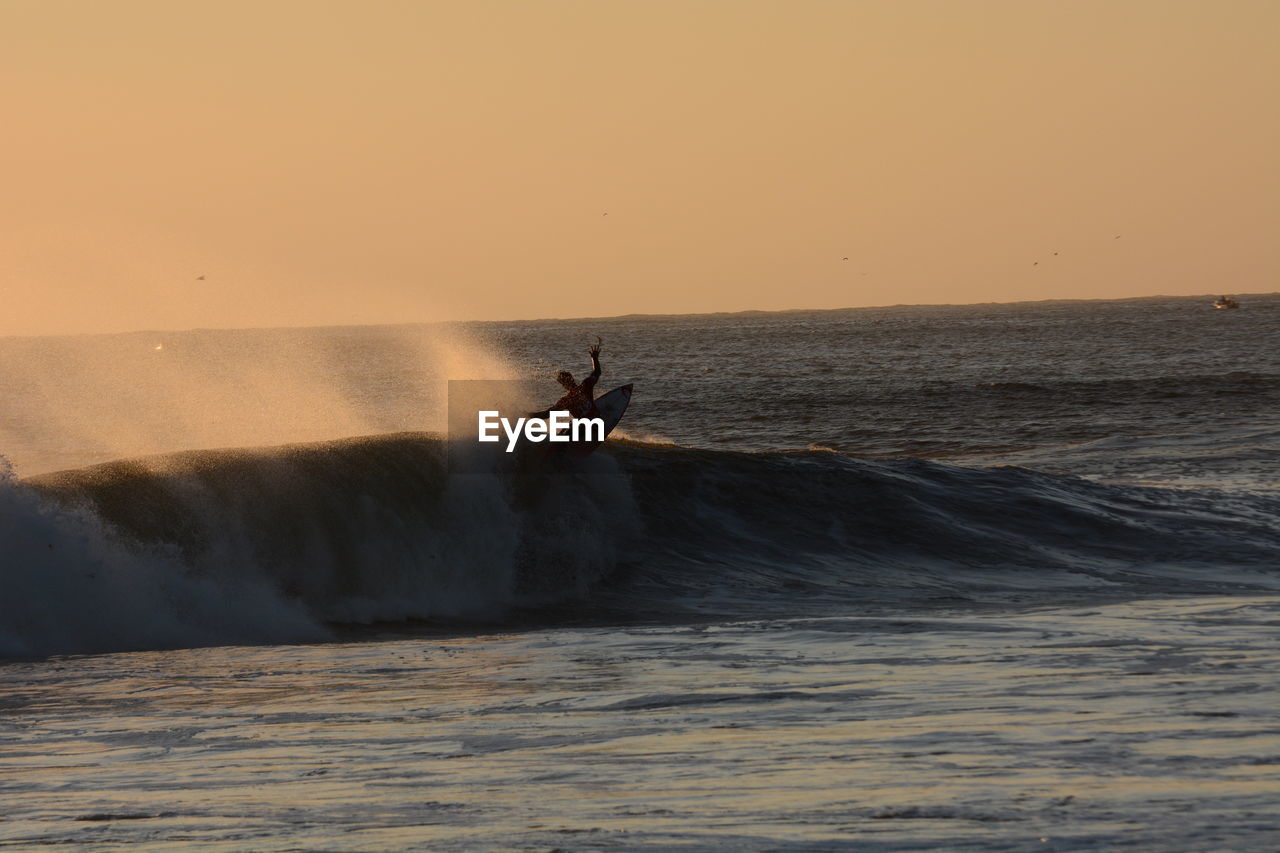 Silhouette man surfing in sea against clear sky during sunset