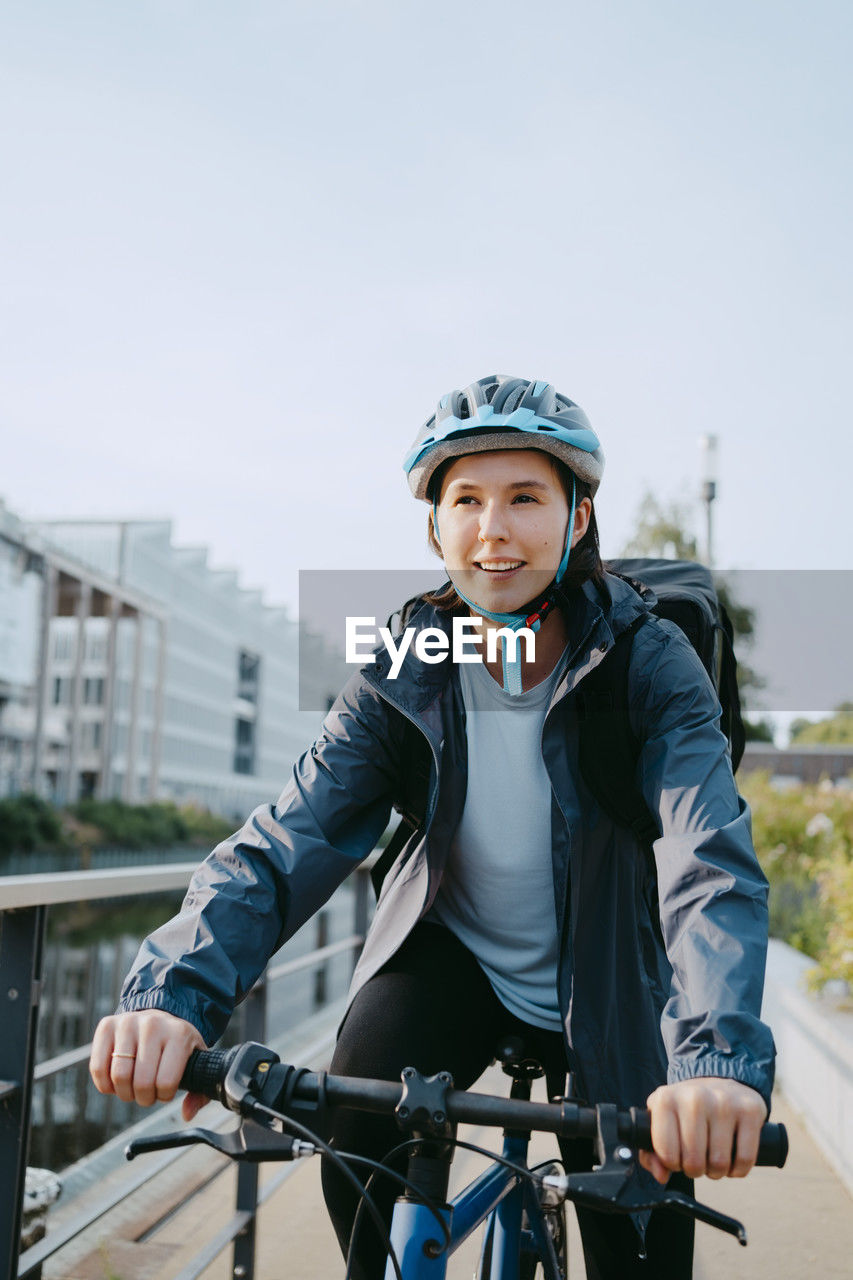 Smiling female delivery person wearing helmet and sitting on bicycle