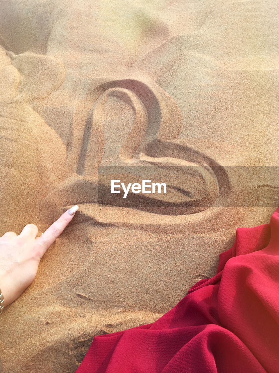 Cropped hand of woman making heart shape on sand at beach