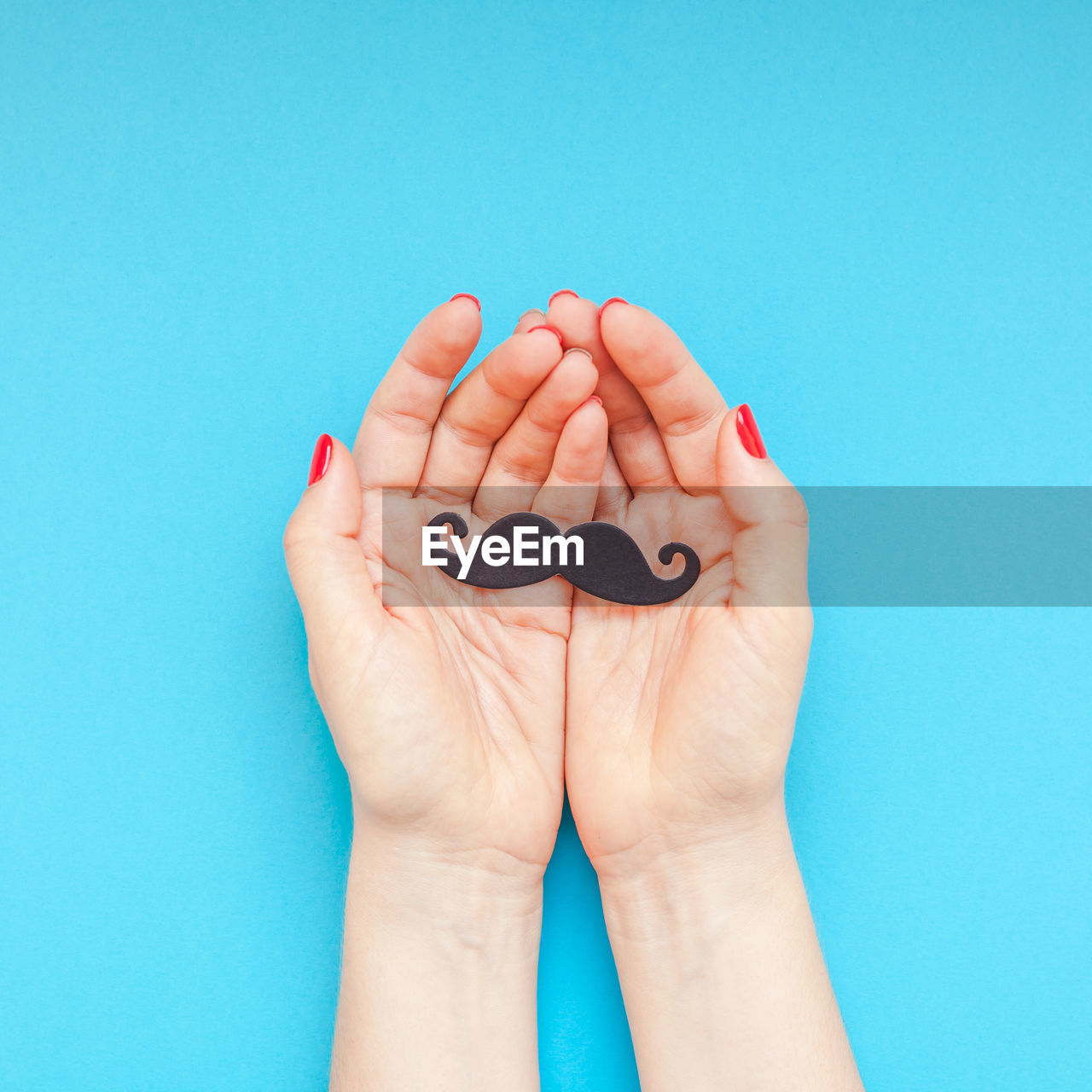 Cropped hands of woman holding party prop against blue background