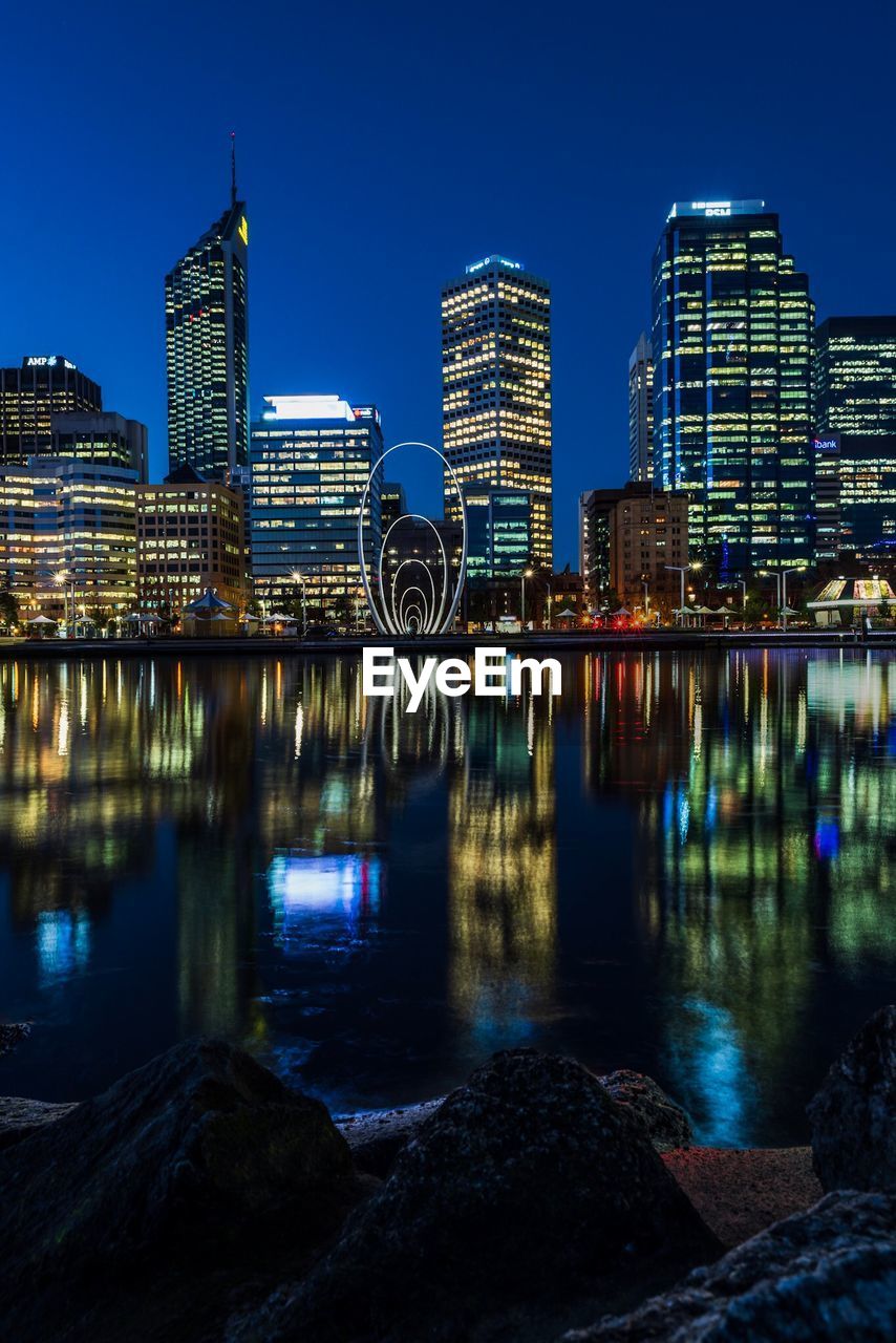 Illuminated buildings by river against sky in city at night