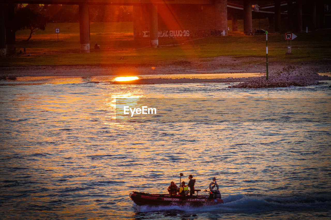 PEOPLE SITTING ON BOAT AT SUNSET