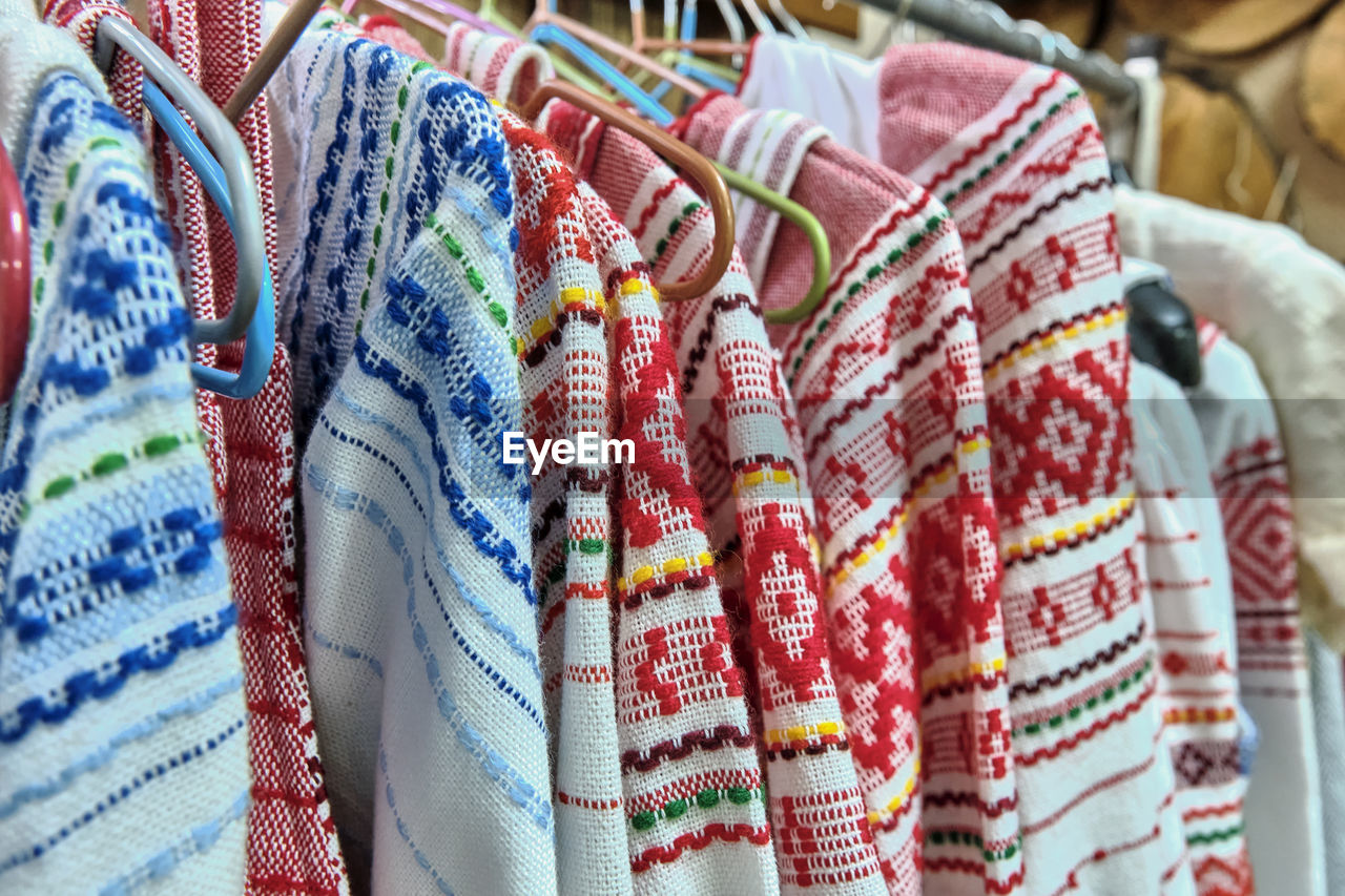 Traditional russian national bright ornaments on woven dresses hanging on hangers.