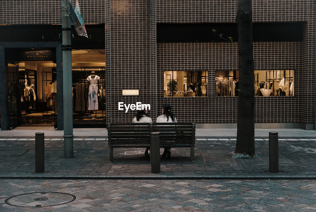 architecture, built structure, seat, building exterior, night, city, adult, lighting, sitting, interior design, urban area, men, bench, full length, street, furniture, illuminated, building, outdoors