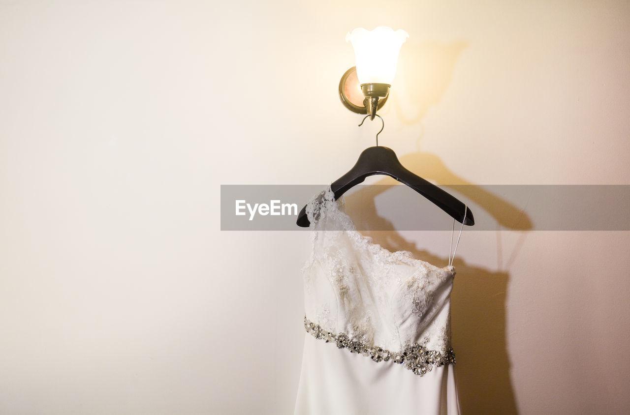 Wedding dress hanging on illuminated lamp by wall