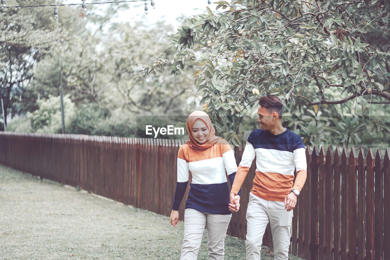 YOUNG COUPLE STANDING BY TREE