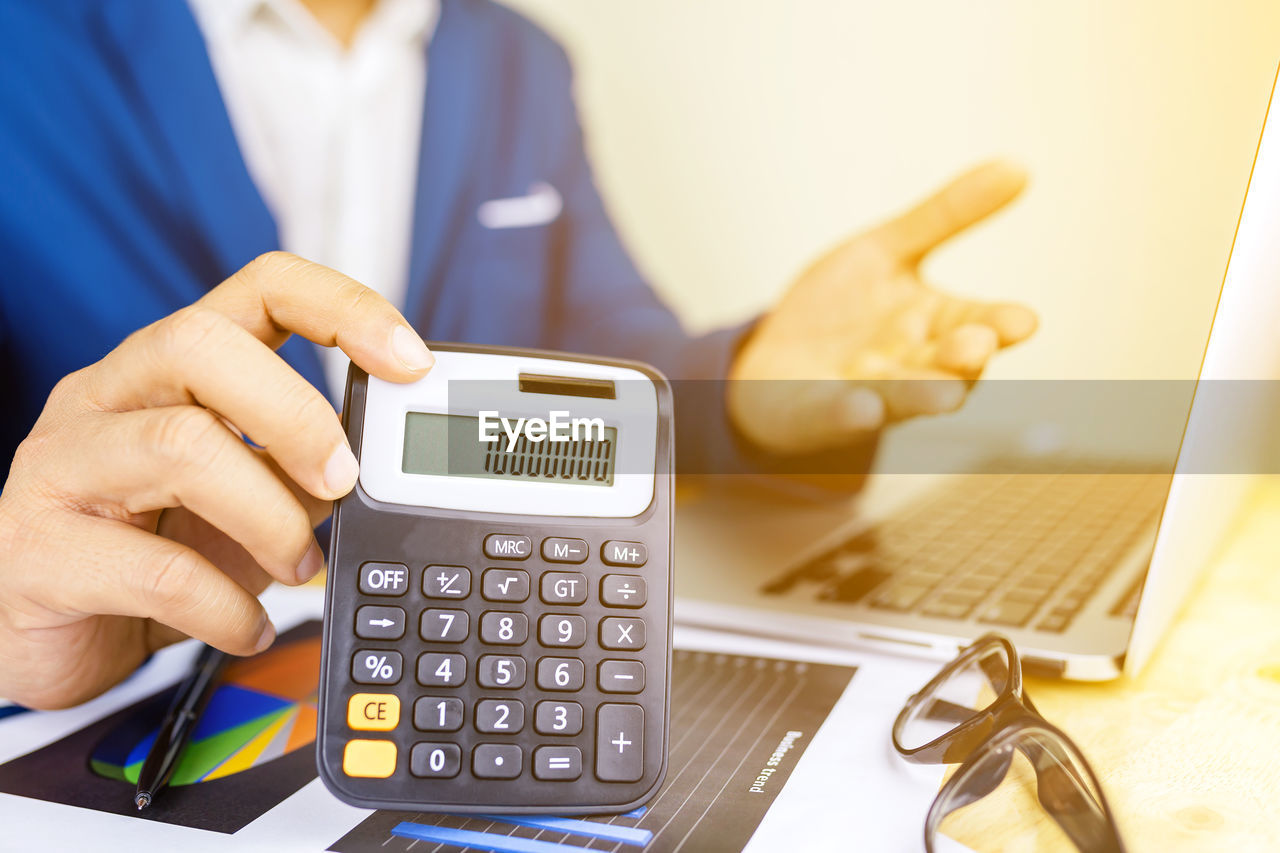 Midsection of businessman showing calculator at desk