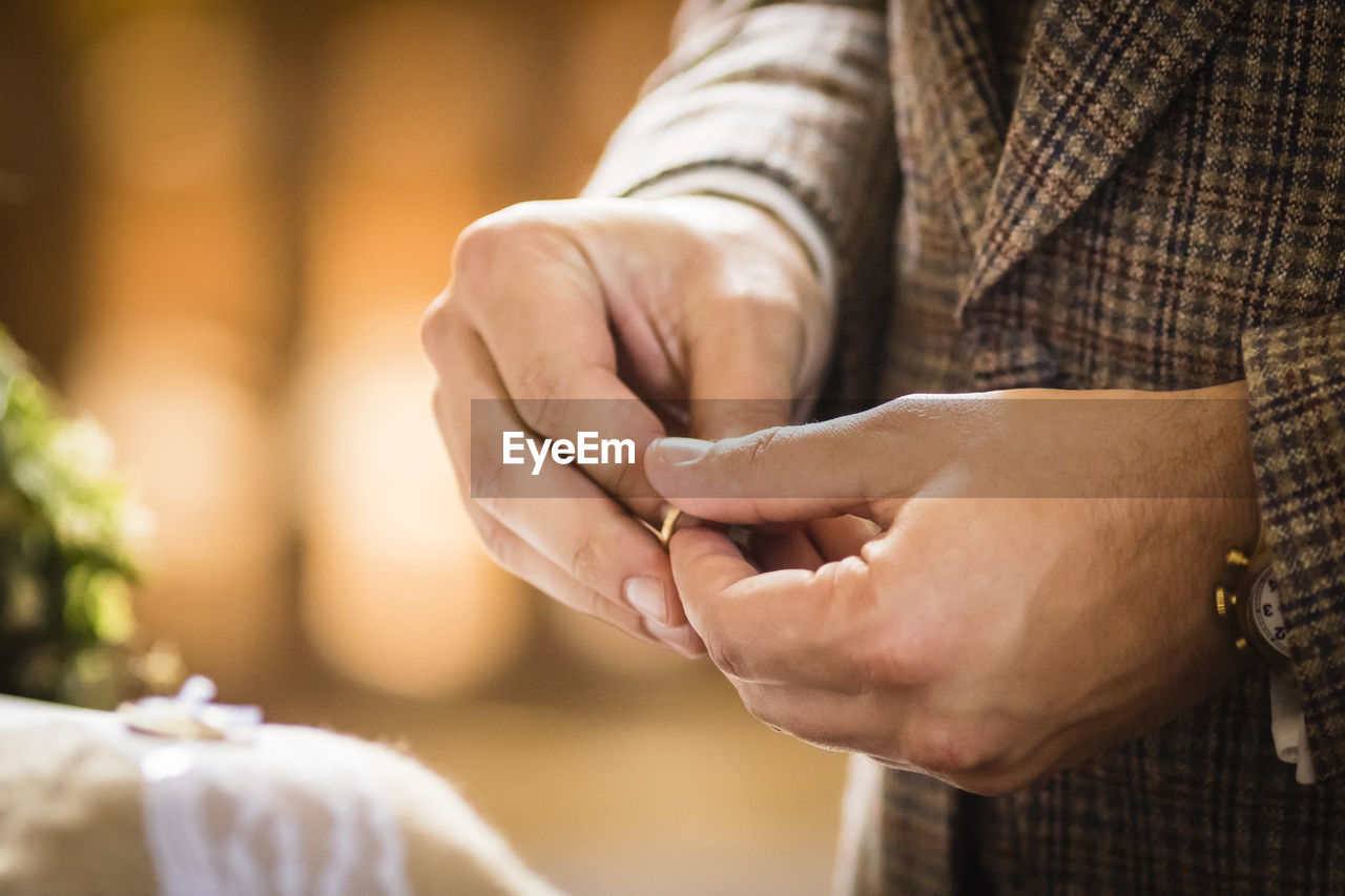 Midsection of bridegroom holding ring during wedding ceremony