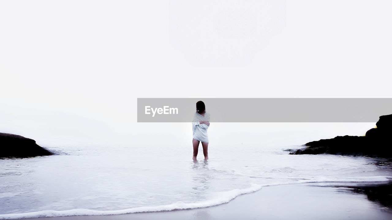 Woman standing at beach against clear sky