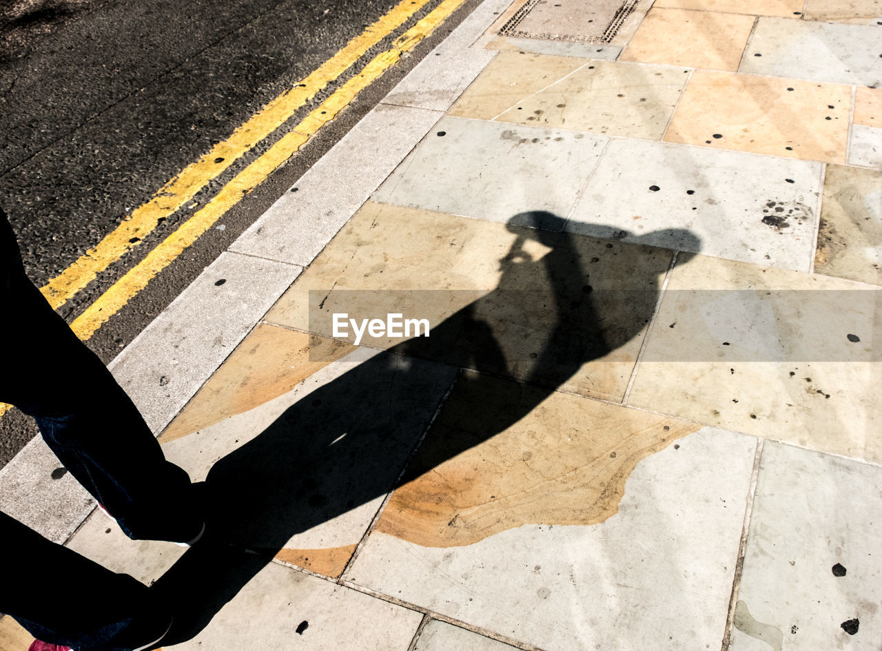 HIGH ANGLE VIEW OF SHADOW OF MAN CROSSING ROAD