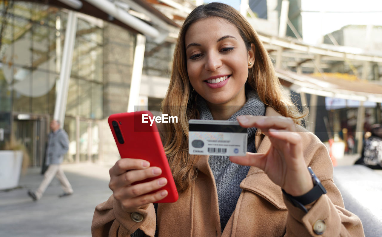 Happy smiling woman holding her smartphone and enters credit card number on winter season outdoors