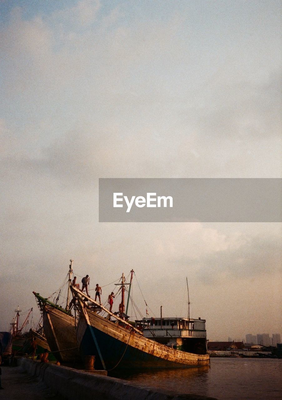 Men on boat moored at harbor against sky