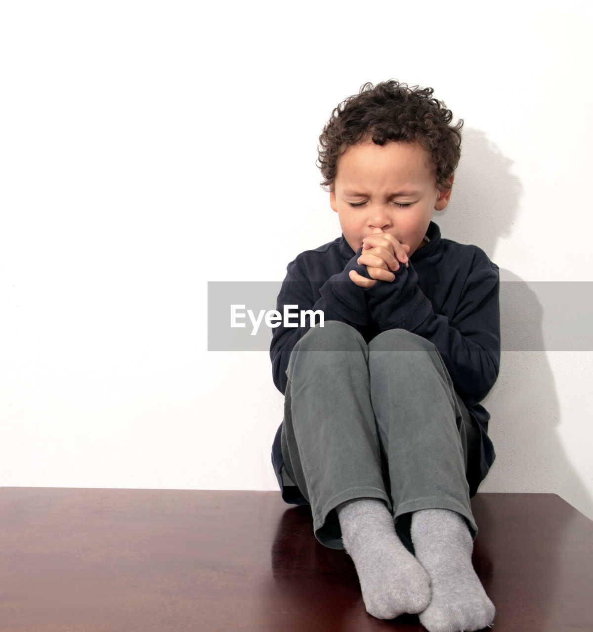 Boy sitting on floor against white background stock photo