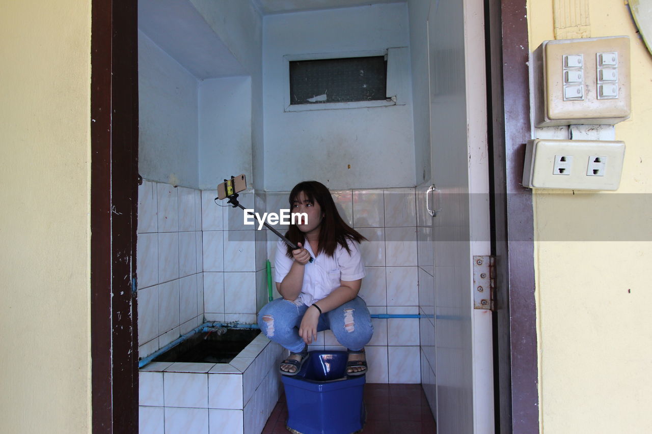 Young woman taking selfie on toilet bowl in bathroom at home