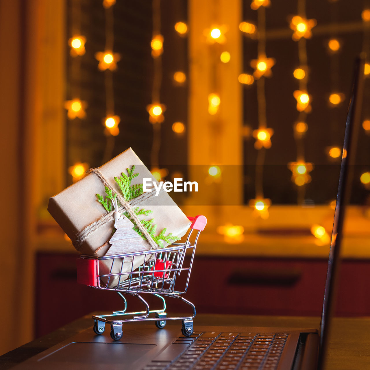 Miniature shopping cart with decorated gift box standing on laptop. concept of on-line shopping