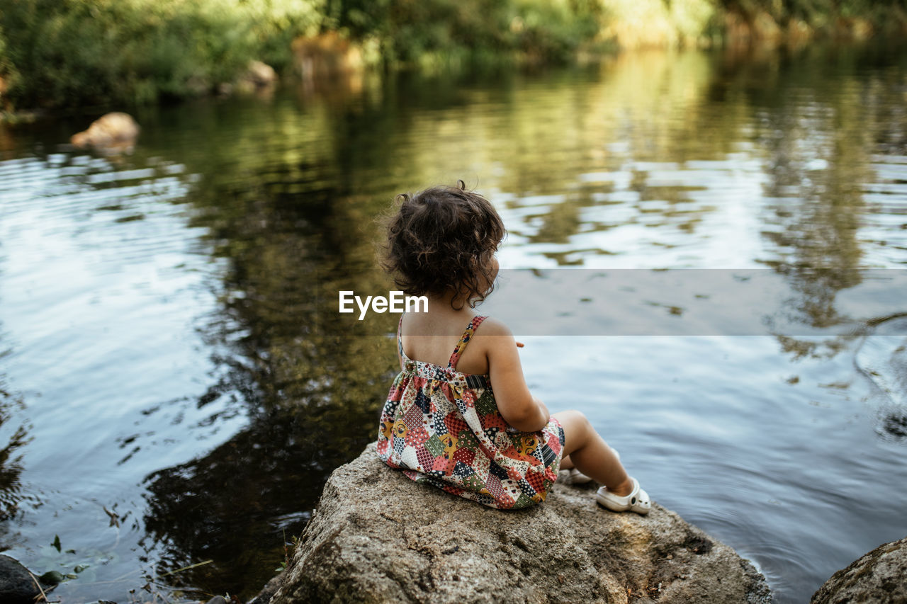 Rear view of woman sitting on rock by lake