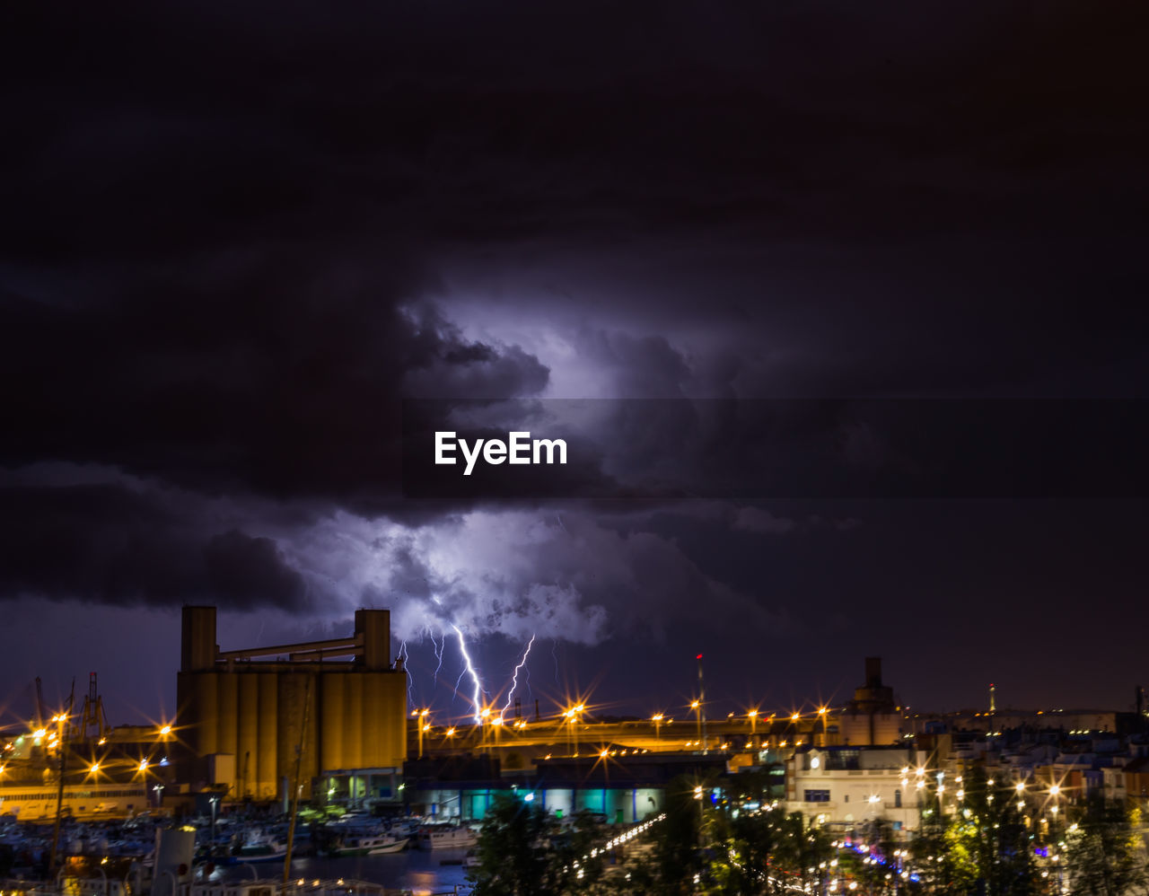 Buildings in city against dramatic sky at night