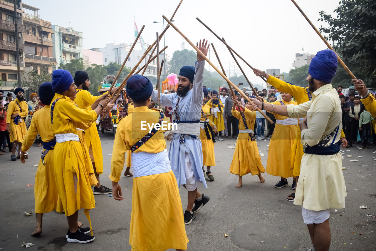 group of people, crowd, city, clothing, tradition, yellow, large group of people, street, architecture, carnival, traditional clothing, men, festival, celebration, performance, arts culture and entertainment, adult, women, person, music, traditional festival, day, dancing, outdoors, event