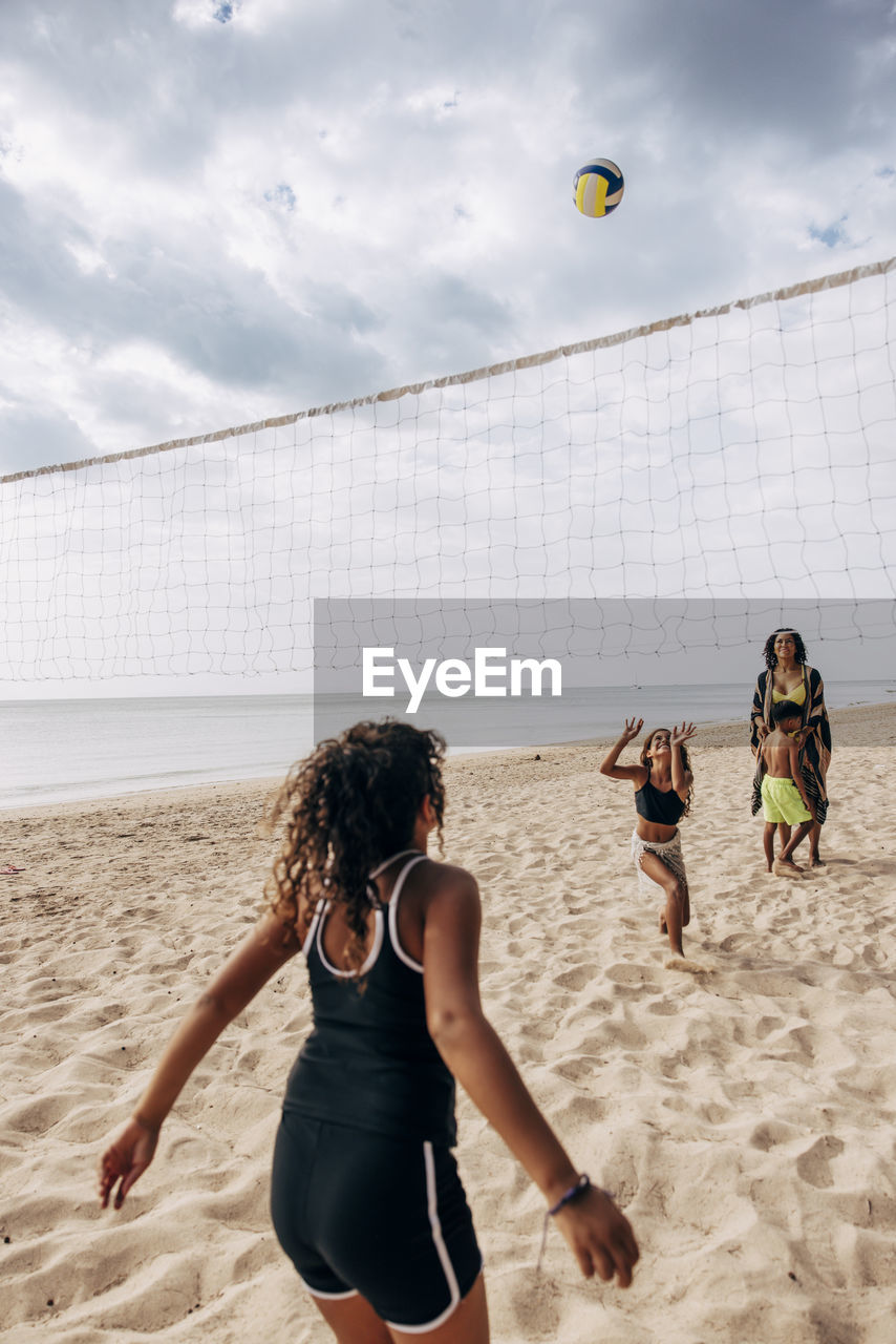 Rear view of girl playing volleyball with family at beach