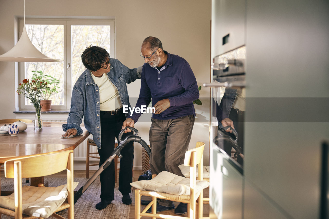 Senior woman talking to man cleaning home with vacuum cleaner